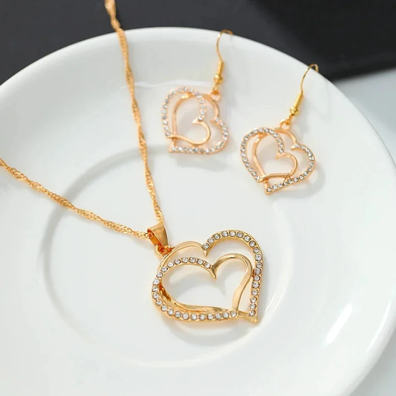A gold necklace and earrings set with double heart pendants, adorned with sparkling crystals.