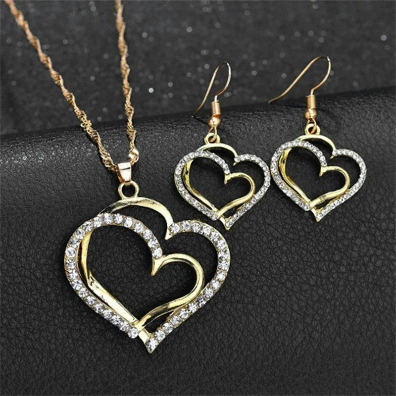 A gold necklace and earrings set with double hearts and clear stones.