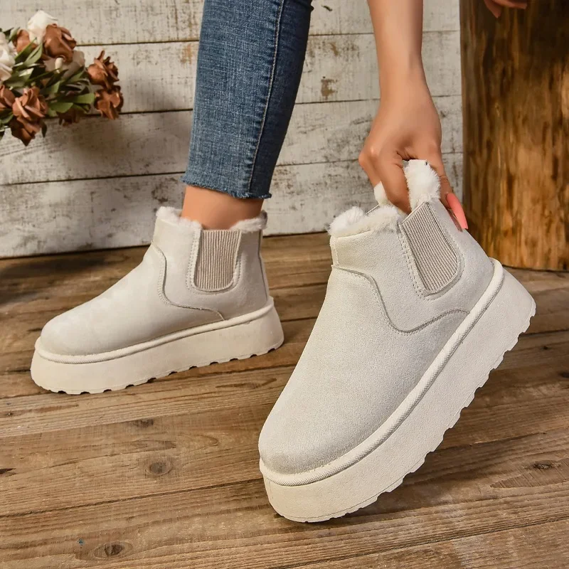 A person's legs and feet are shown wearing a pair of light beige ankle boots with thick white soles. The boots are made of suede and have a fuzzy lining. The person is wearing jeans and is holding one of the boots.