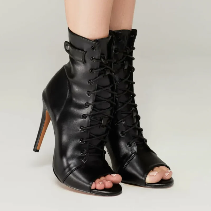 A pair of black peep-toe lace-up boots are shown on a model's feet. The boots have a stiletto heel and are made of leather.