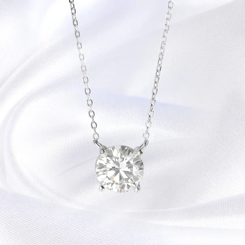 A stunning solitaire diamond pendant necklace rests on a white silk background. The pendant features a large, round-cut diamond that is brilliantly cut and sparkles with exceptional fire and brilliance. The necklace is made of delicate white gold chain and features a simple, elegant design that allows the diamond to take center stage. The overall aesthetic is one of luxury and sophistication.
