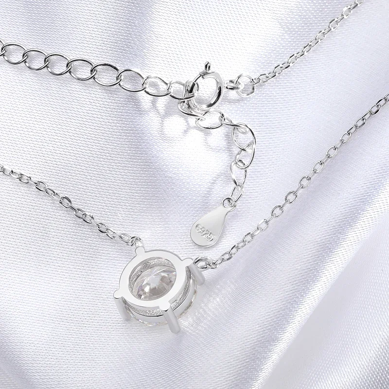 Close-up view of a silver necklace with a clear gemstone pendant resting on a white fabric background.