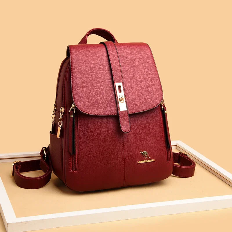 A maroon leather backpack with gold accents sits on a beige surface.