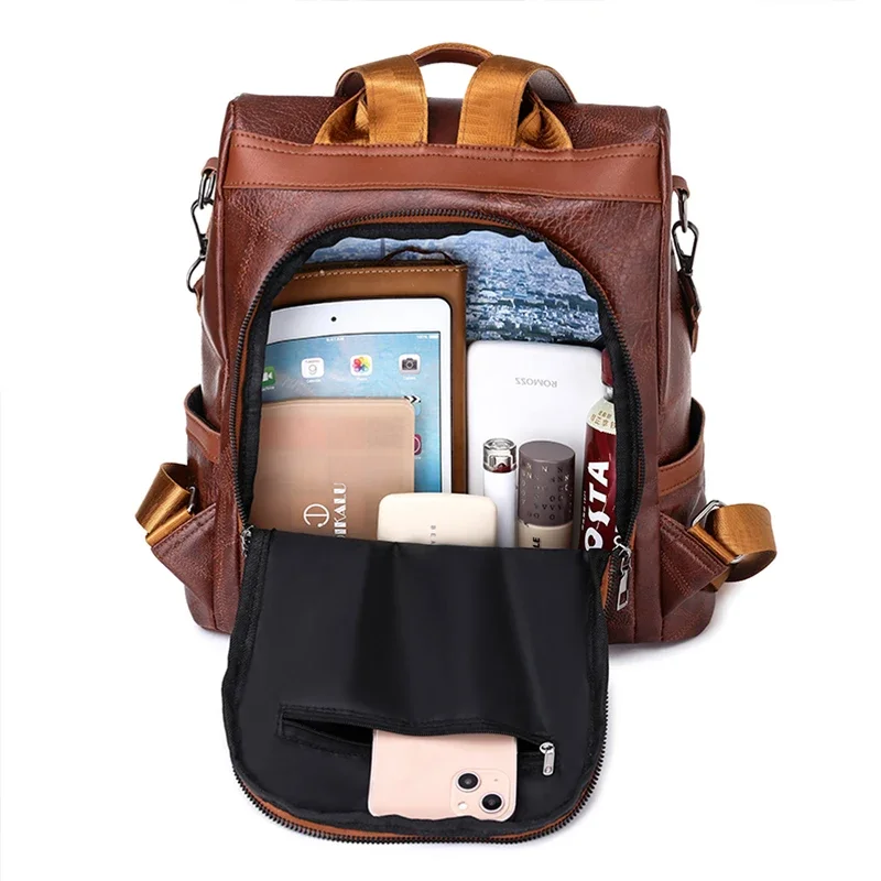 A brown leather backpack is open, revealing its many compartments and pockets. Various items are neatly organized inside, including a tablet, phone, wallet, and makeup. The backpack is stylish and functional, perfect for everyday use.