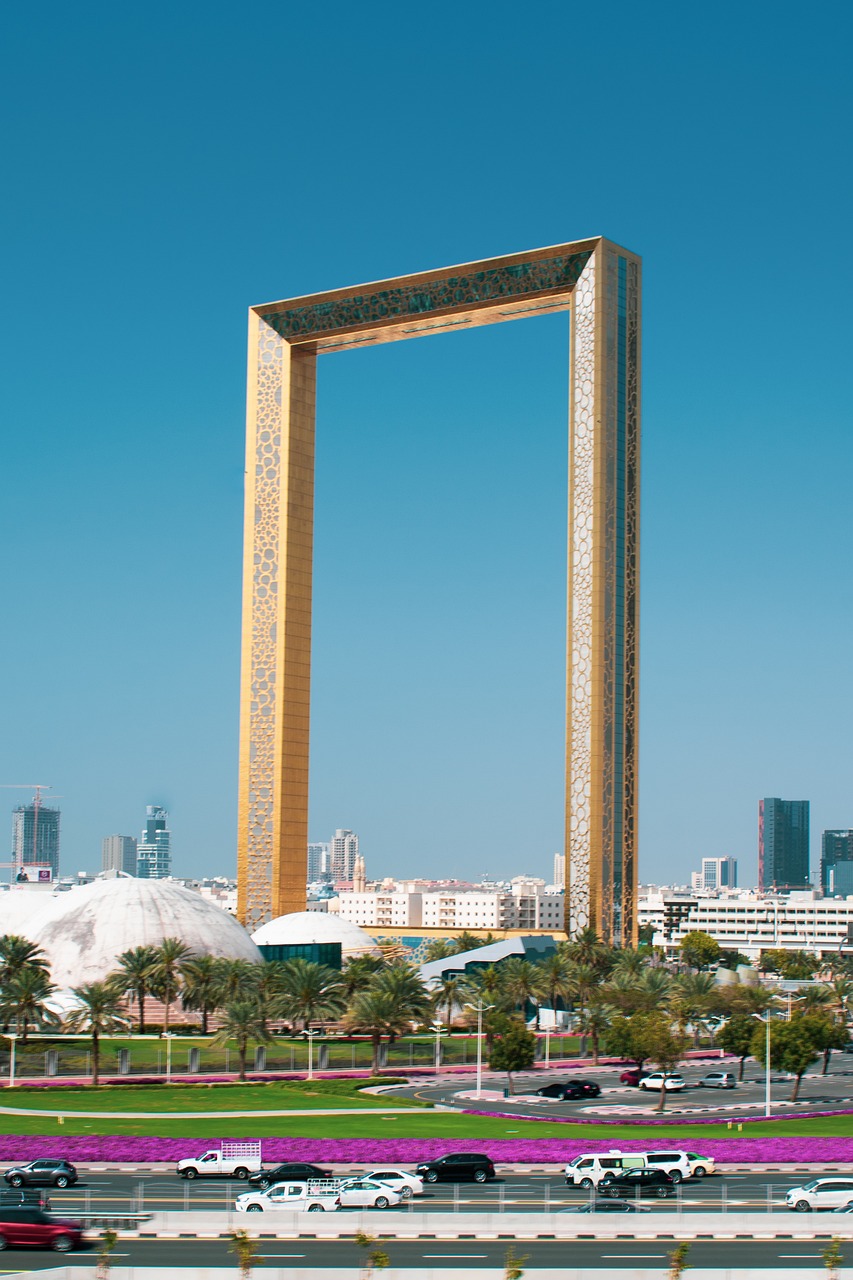 The Dubai Frame, a towering golden rectangular structure, standing against a clear blue sky with a vibrant cityscape in the background.
